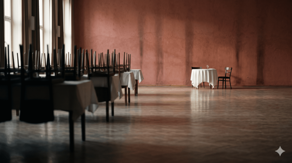 An empty mid-century hotel ballroom with a small isolated white-linen table set against a red-ochre wall, reflecting Hattie McDaniel's 1940 Oscar night.