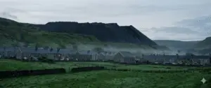 Cinematic full-frame view of a green Welsh mining valley at dawn with terraced houses and a dark coal spoil tip on the hillside.
